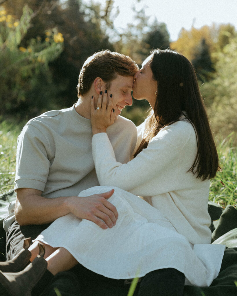 Girl kisses boy's forehead showing off ring in Vermont engagement photos, by Elsie Goodman Photography.