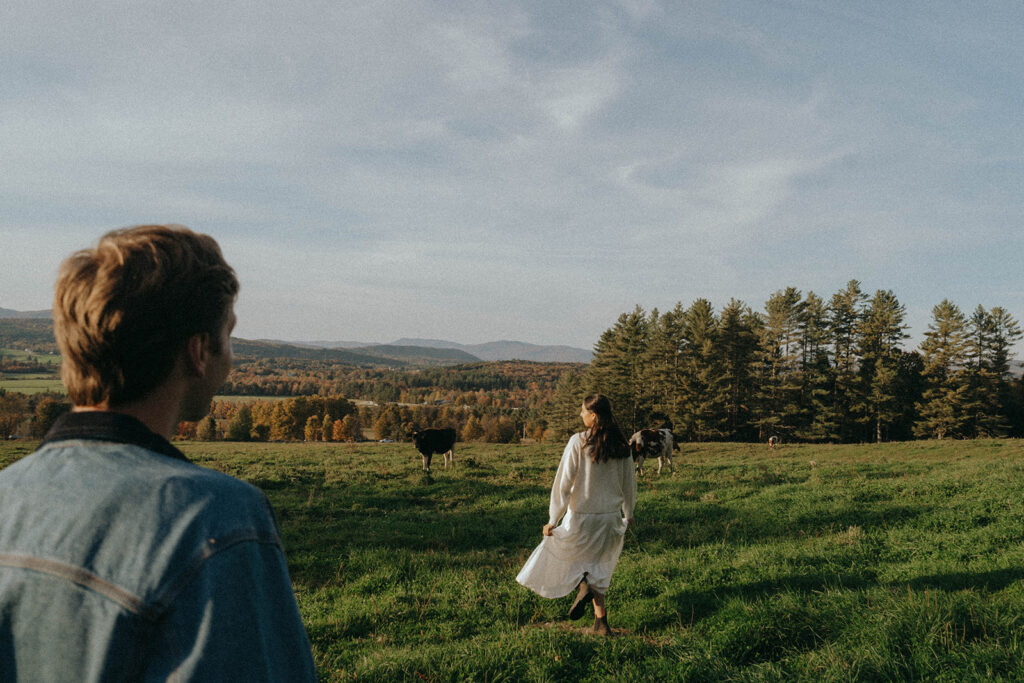 Couple walking in grassy meadow with cows and showcasing Autumn in Vermont, by Elsie Goodman.