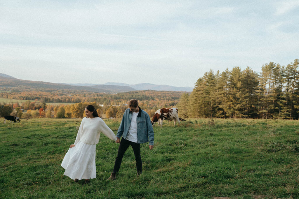 Walking hand-in-hand in a Vermont field, couple smiles during fall engagement session, photo by Elsie Goodman.