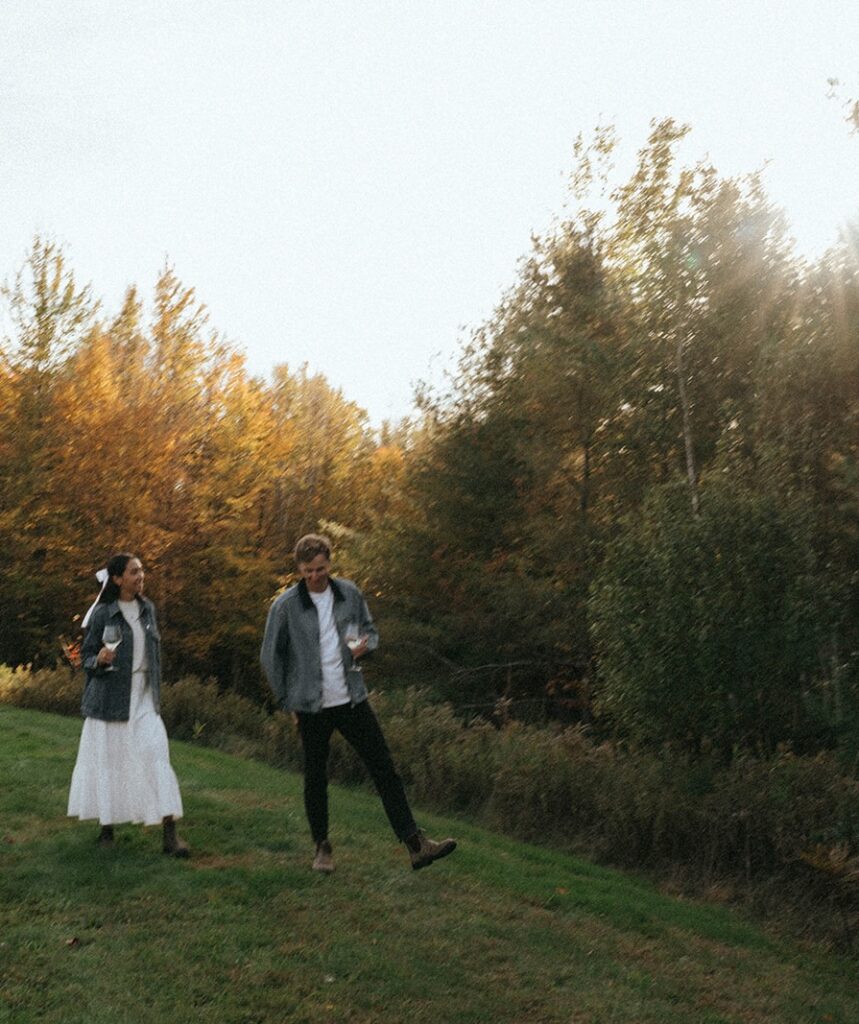 Couple at an engagement session in Vermont walking with wine, shot by Elsie Goodman Photography.