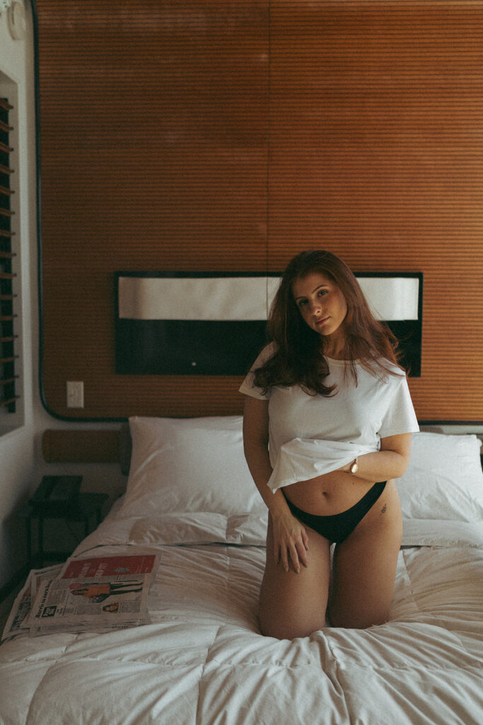 Hotel boudoir photos of woman kneeling on bed in white t-shirt and black lingerie, shot by Elsie Goodman Photography.