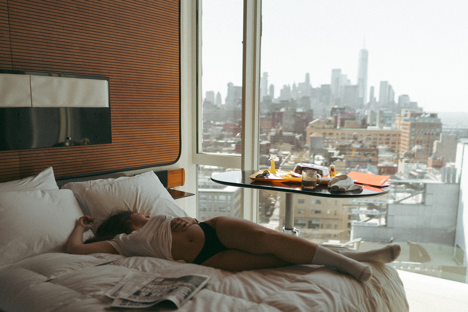 Morning hotel boudoir photos of woman relaxing in bed with city skyline view, shot by Elsie Goodman Photography.
