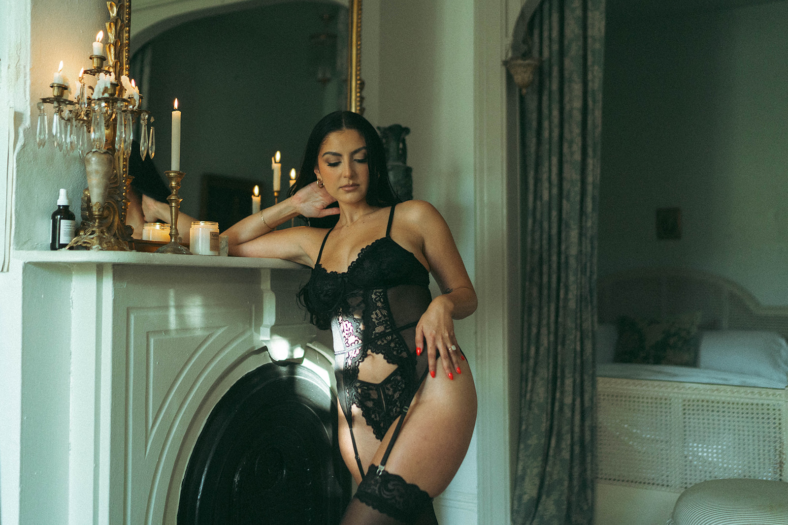 Woman in black lace lingerie standing by a vintage fireplace with candles during a boudoir photoshoot at home, shot by Elsie Goodman Photography.