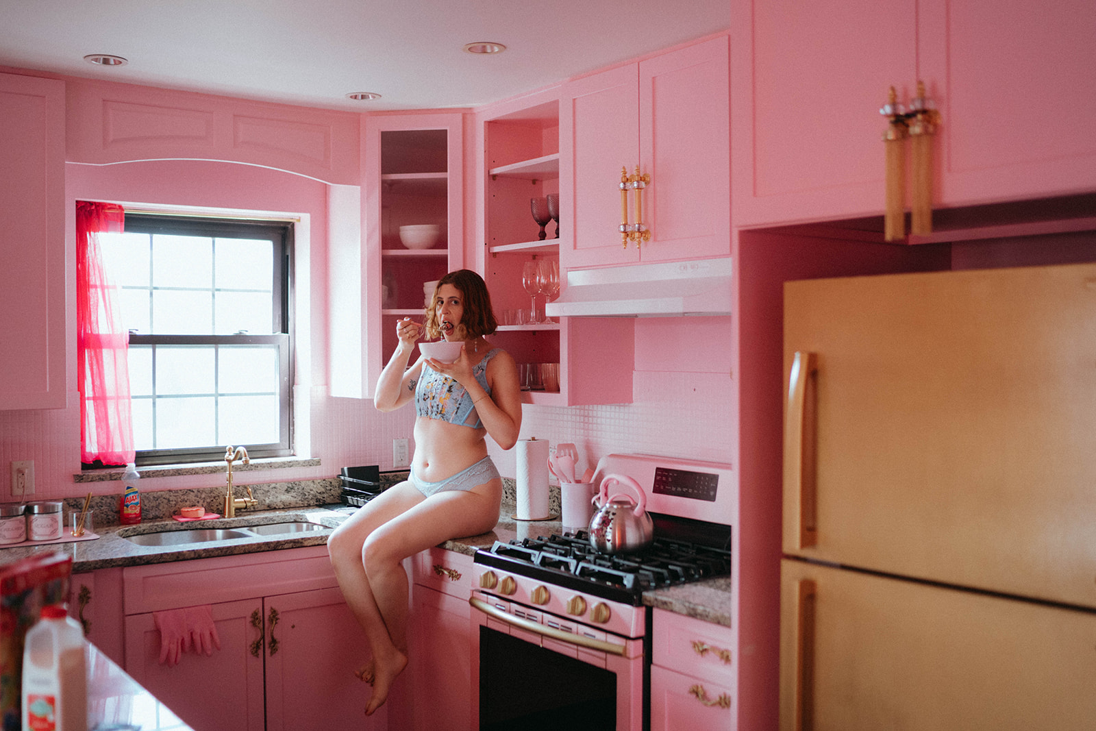 Amateur housewife boudoir photography in a retro pink kitchen with natural light, showcasing playful pink boudoir photography style by Elsie Goodman Photography