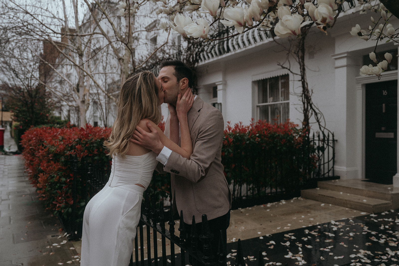 A man and women kissing in a damp London street. A magnolia tree and house behind them, shot by London engagement photographer Elsie Goodman.