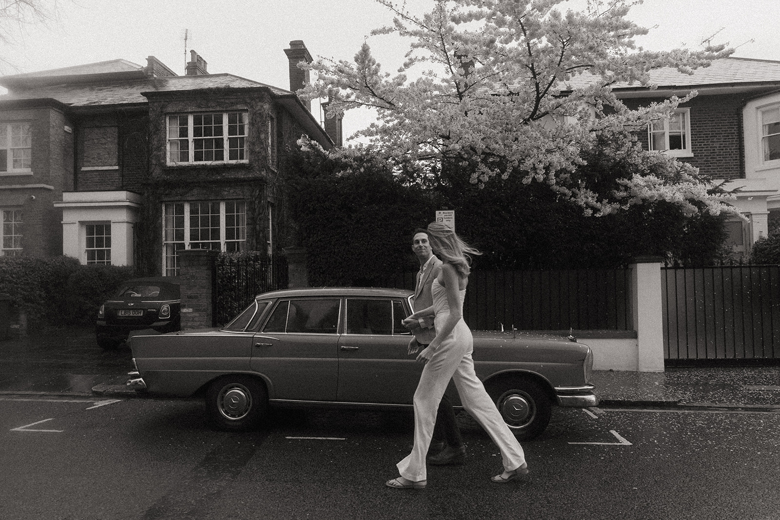 Black and white photos of a man and women walking, hand in hand, down a street in front of a vintage car, shot by London engagement photographer Elsie Goodman.