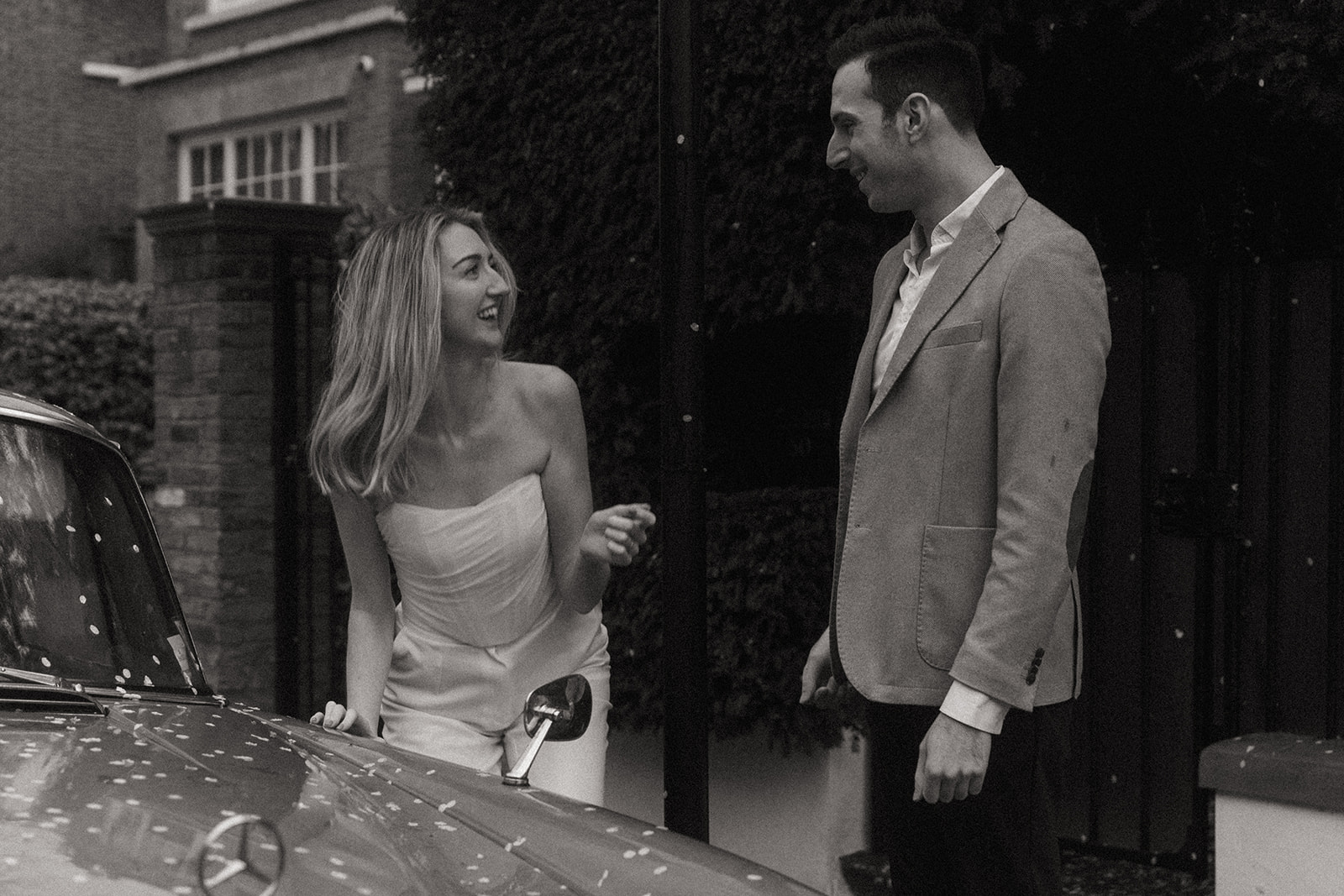 Man and women smiling at each other, there are petals all over a vintage Mercedes, shot by London engagement photographer Elsie Goodman.