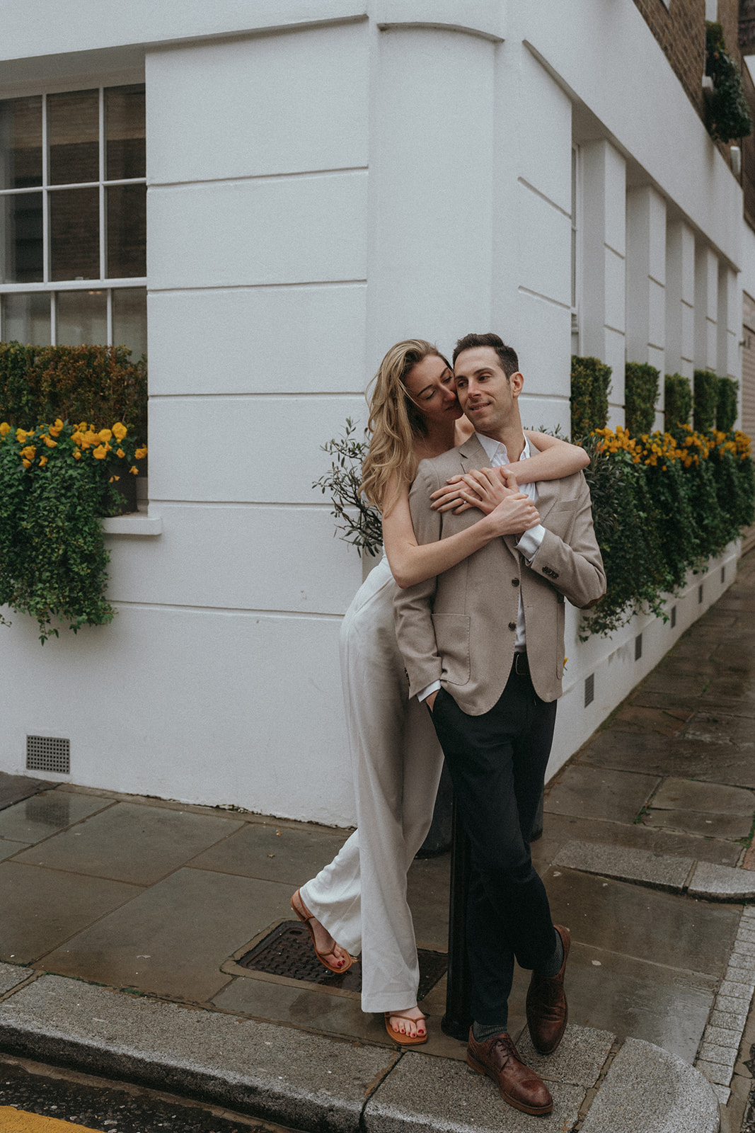 A woman standing behind her fiancé with her arms wrapped around him lovingly on a London corner, shot by London engagement photographer Elsie Goodman.