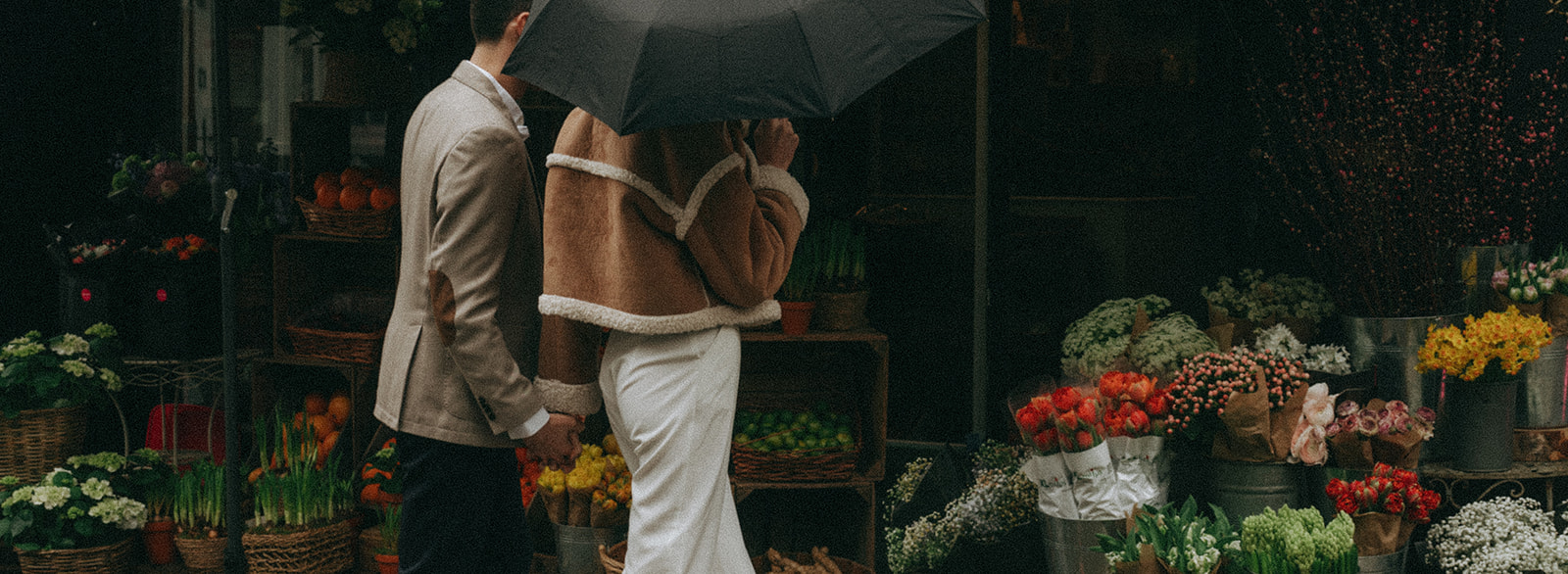 Wide angle shot of a man and a woman holding hands outside a London flower shop, shot by London engagement photographer Elsie Goodman.