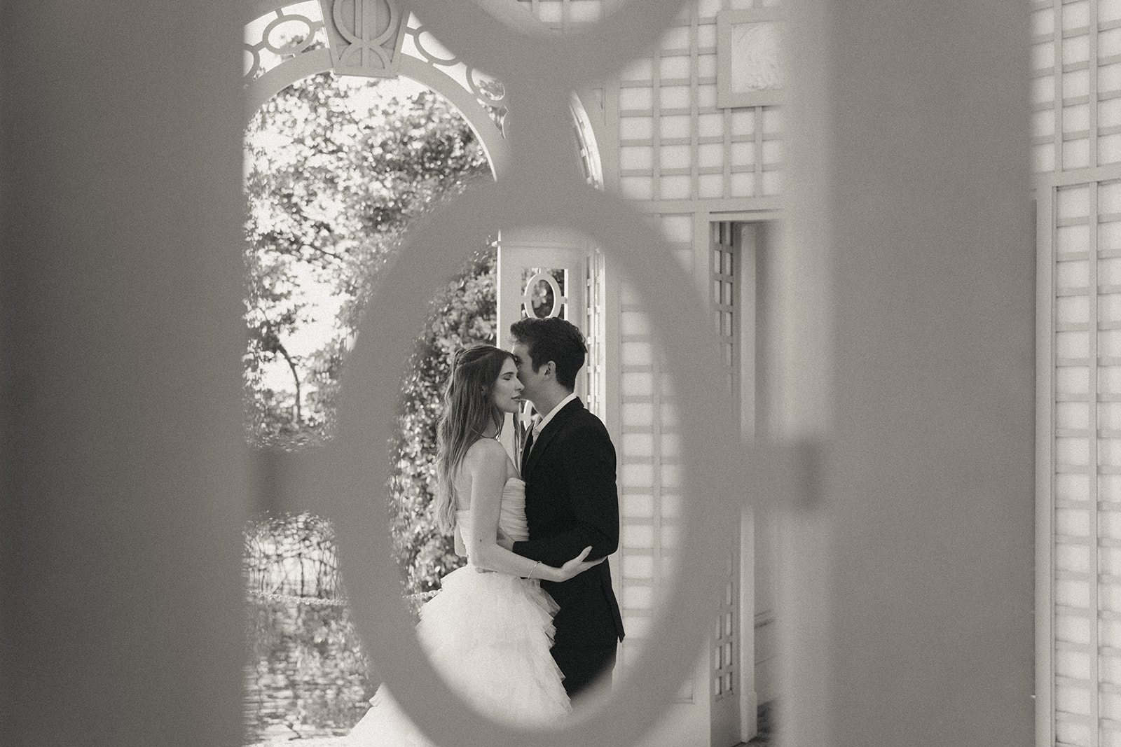 Viscaya Black and White photo of a bride and groom leaning into each other, taken through a garden fence by Vizcaya Wedding Photographer Elsie Goodman.