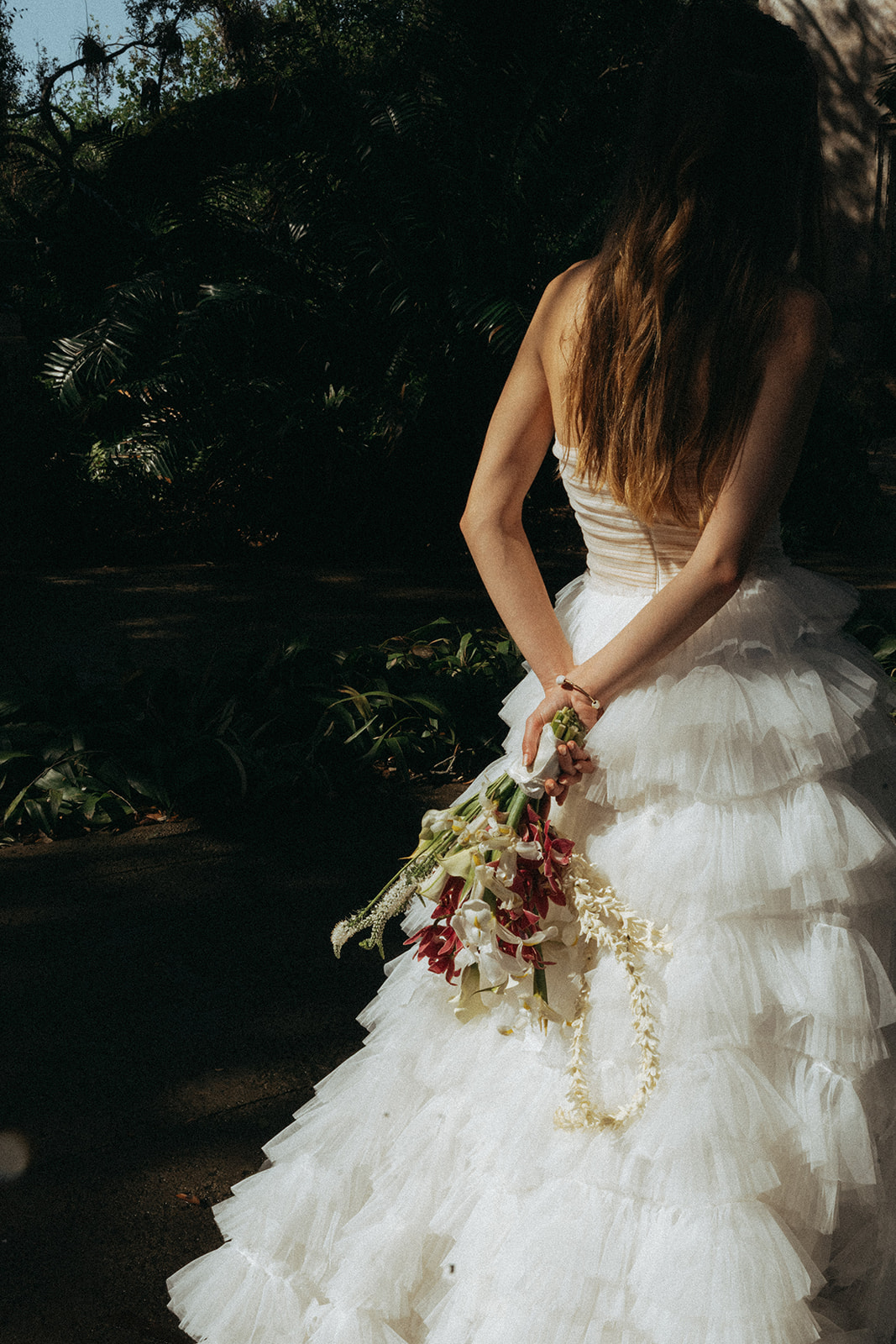 Viscaya Bride holds her bouquet behind her with both hands, the background is dark by Vizcaya Wedding Photographer Elsie Goodman.
