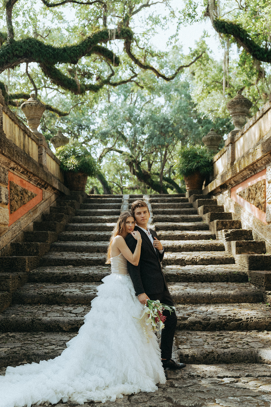 Viscaya Bride holds the groom from behind, they are both looking seriously at the camera by Vizcaya Wedding Photographer Elsie Goodman.