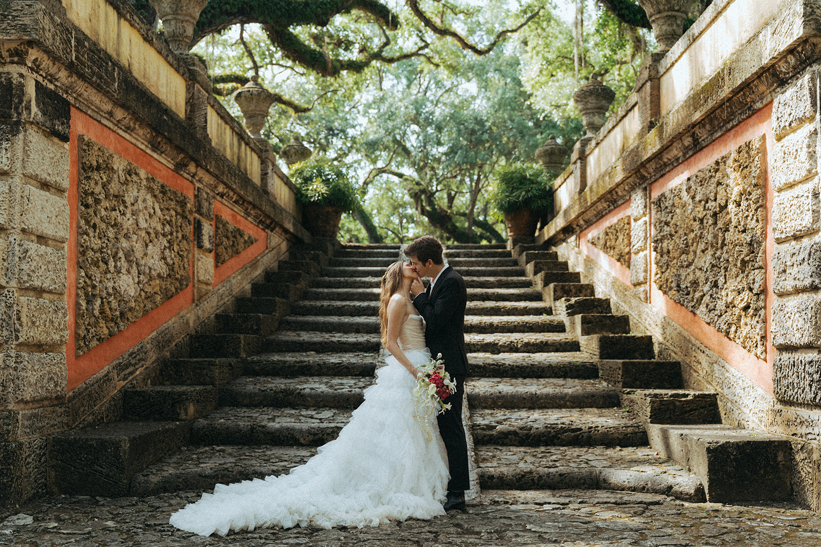 Viscaya Bride and groom kiss in front of a large outdoor staircase by Vizcaya Wedding Photographer Elsie Goodman.