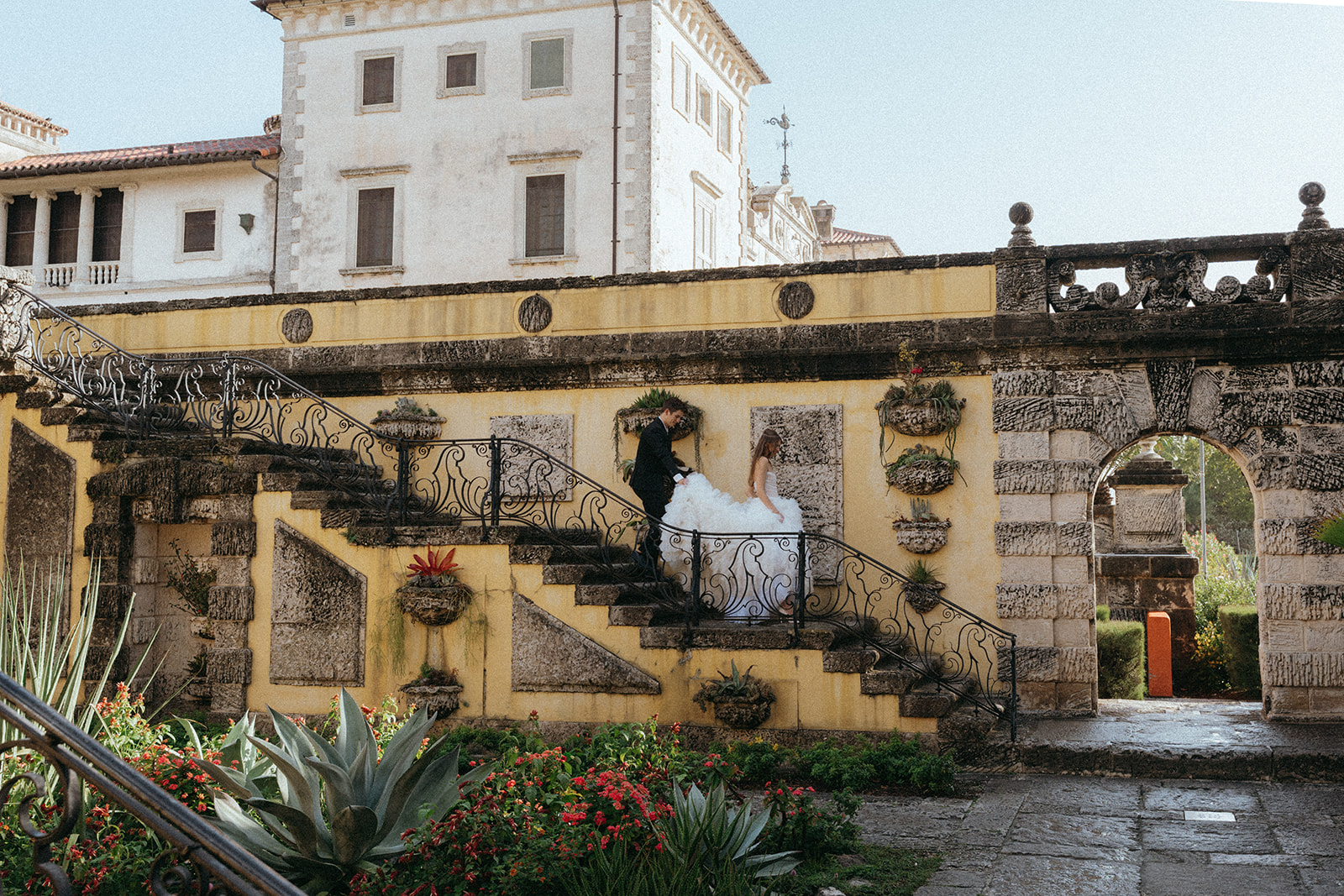 Viscaya Groom helps with brides dress as she walks down some stairs by Vizcaya Wedding Photographer Elsie Goodman.