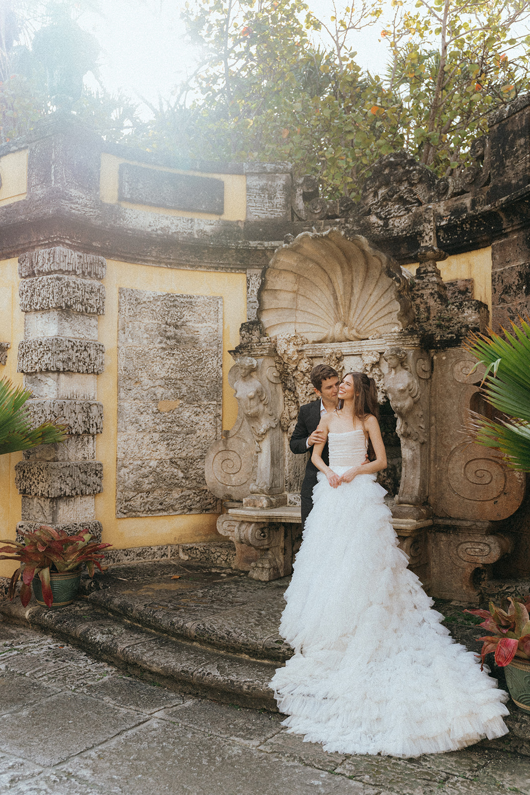 Viscaya Groom stands behind his bride kissing her by Vizcaya Wedding Photographer Elsie Goodman.