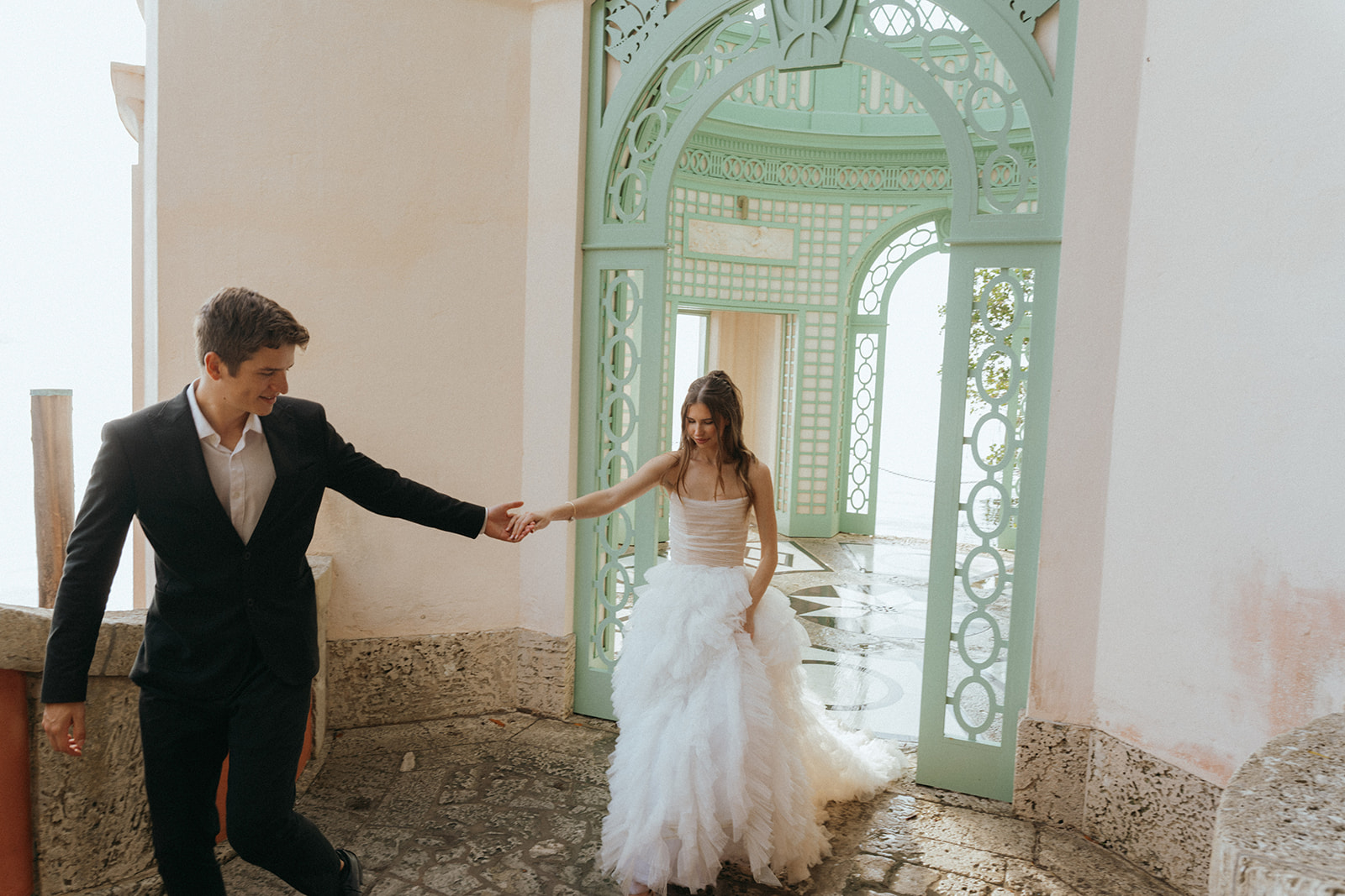 Viscaya The bride takes the hand of her groom walking up some stairs by Vizcaya Wedding Photographer Elsie Goodman.