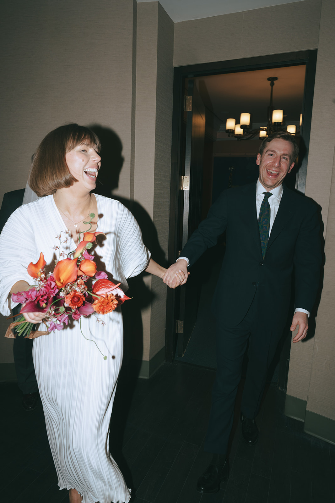 Rachel and Dave’s 2 day celebration Bride and groom walking though the doorway hand-in-hand smiling, laughing by NYC city hall wedding photographer Elsie Goodman.
