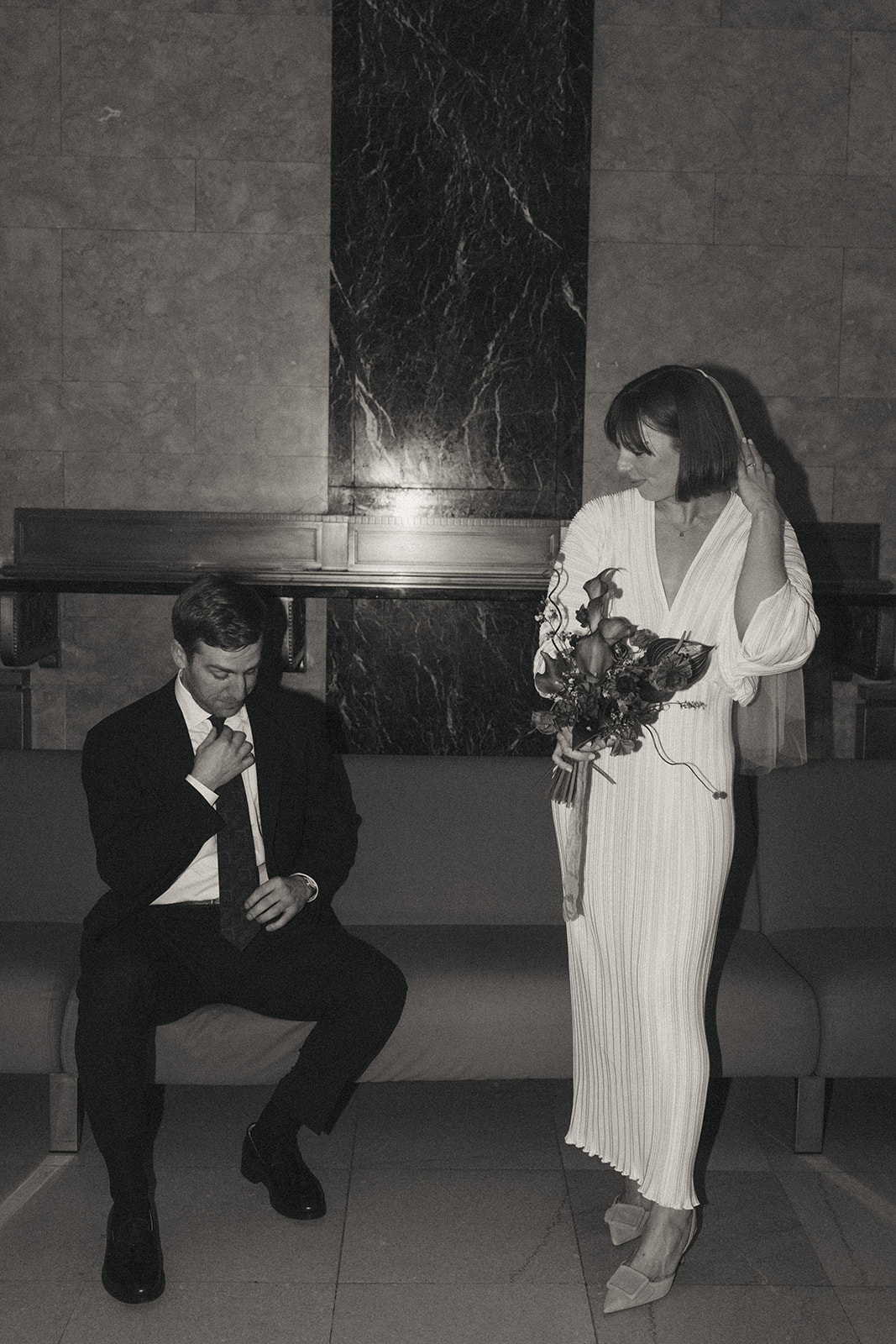 Rachel and Dave’s 2 day celebration Black and white photo of a groom sitting, looking down at his tie, the bride adjusts her veil looking at him by NYC city hall wedding photographer Elsie Goodman.