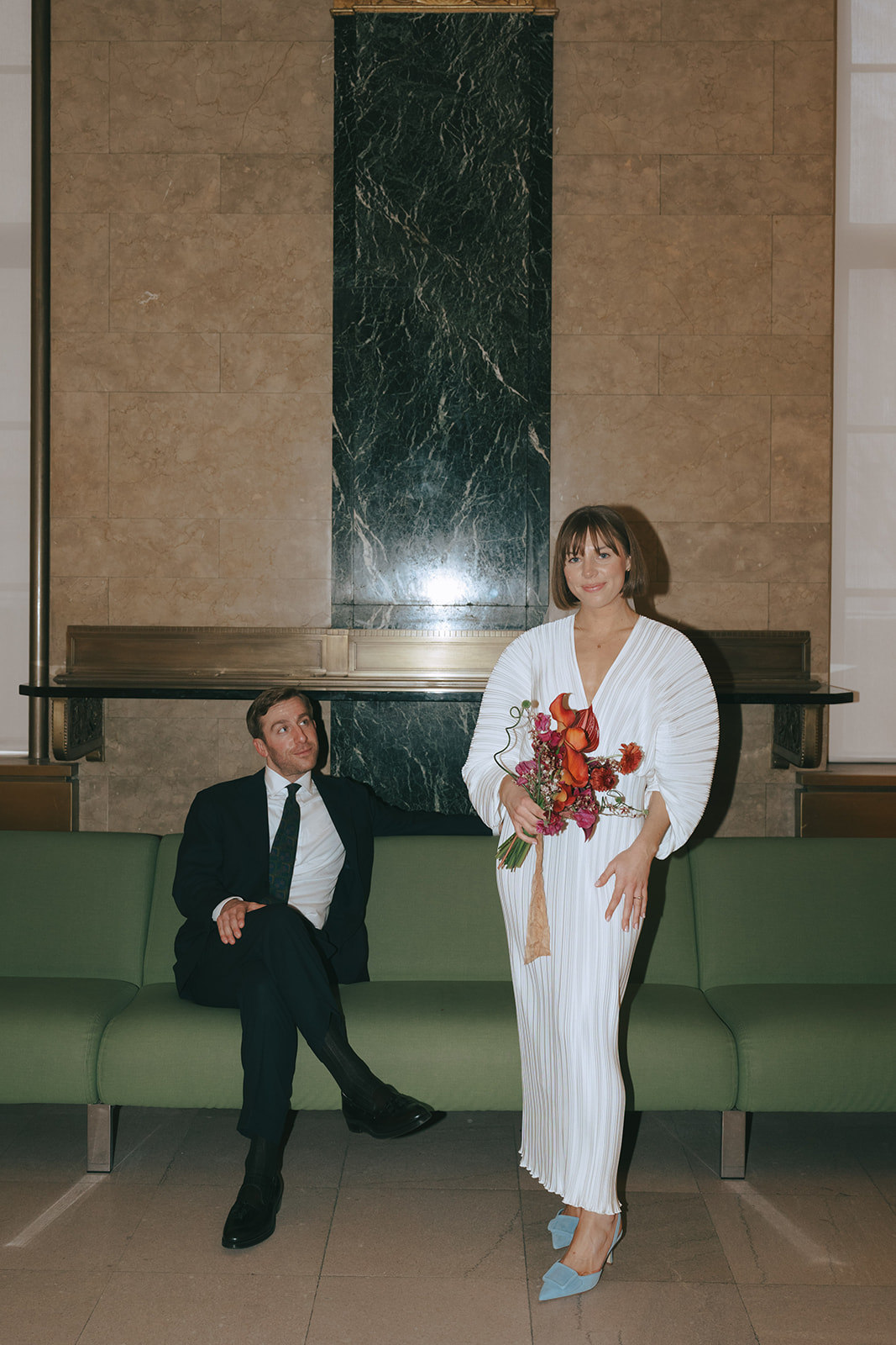 Rachel and Dave’s 2 day celebration Groom sits, looking at his bride as she stands in a vintage wedding dress holding her bouquet by NYC city hall wedding photographer Elsie Goodman.