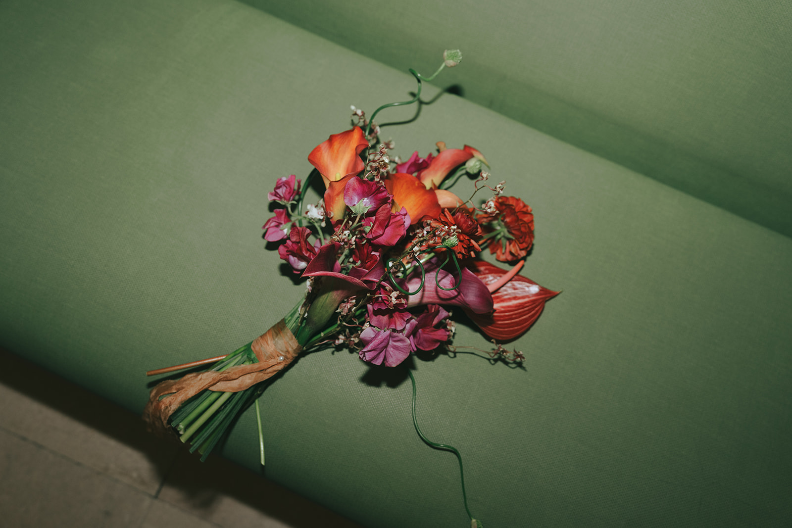 Rachel and Dave’s 2 day celebration Orange, purple and green bridal bouquet on a green couch by NYC city hall wedding photographer Elsie Goodman.