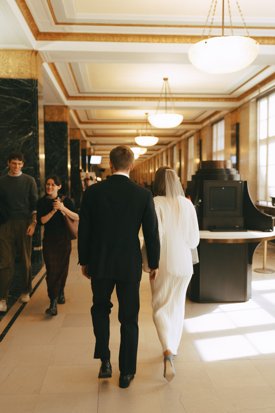Rachel and Dave’s 2 day celebration Bride and groom walking down a hallway by NYC city hall wedding photographer Elsie Goodman.