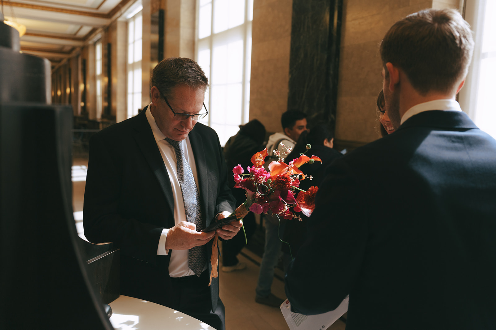 Rachel and Daves 2 day celebration Man hold a wedding bouquet and looks at his phone by NYC city hall wedding photographer Elsie Goodman.