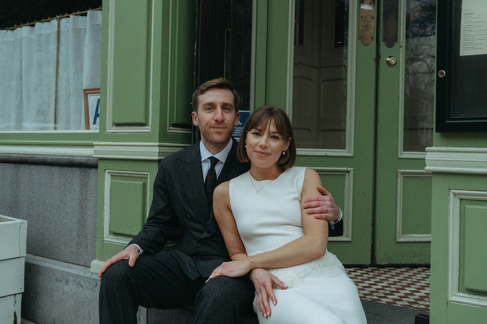 Rachel and Dave’s 2 day celebration Bride and groom leaning into each other look directly at the camera as they sit on the step in front of Franks NYC by NYC elopement photographer Elsie Goodman.
