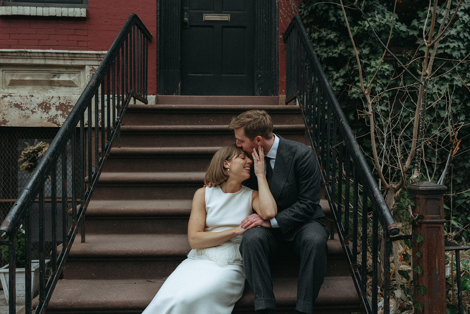 Rachel and Dave’s 2 day celebration Bride and groom sitting on a stoop in NYC, the groom kisses the brides forehead by NYC elopement photographer Elsie Goodman.