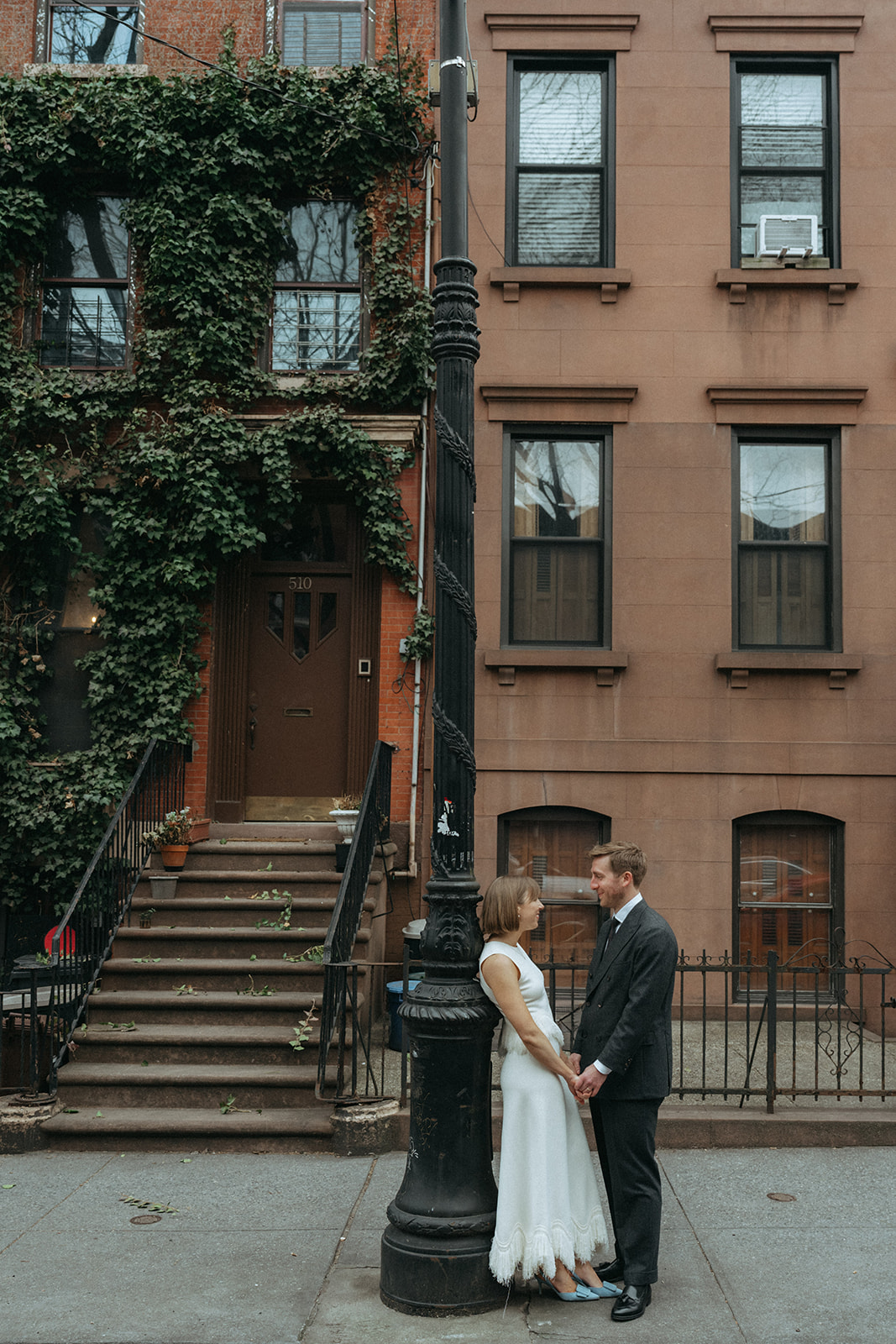 Rachel and Dave’s 2 day celebration Bride leans against a light pole in a vintage wedding dress while holding the grooms hands by NYC elopement photographer Elsie Goodman.