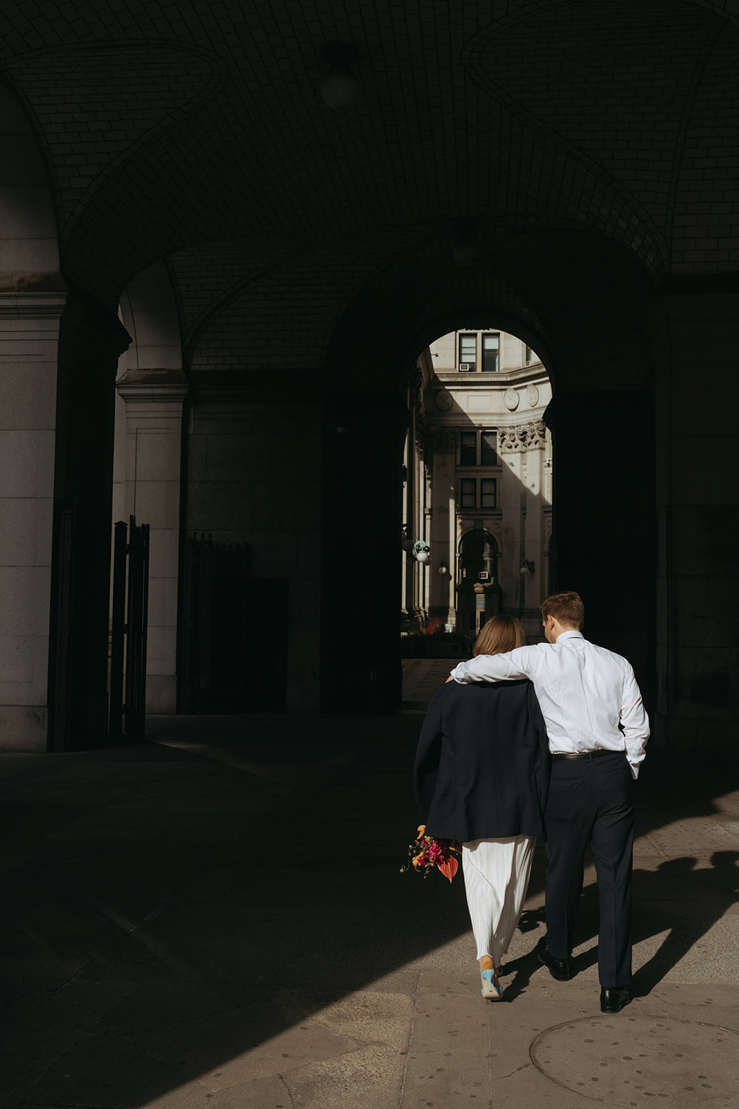 Rachel and Dave’s 2 day celebration Bride and groom walking away from the camera, he has his arm around her shoulders, she is wearing his suit jacket by NYC city hall wedding photographer Elsie Goodman.