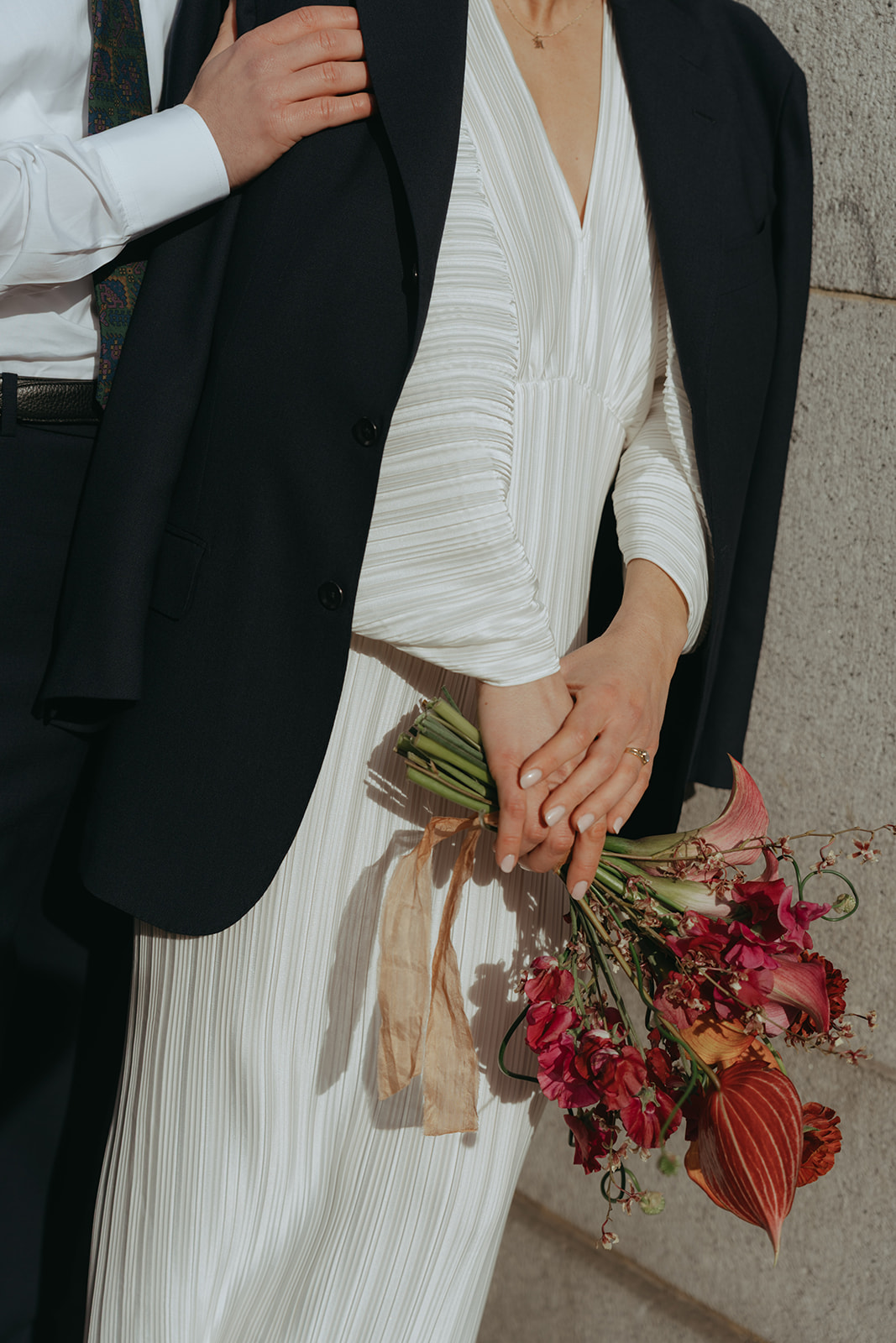 Rachel and Dave’s 2 day celebration Bride with the groom's jacket over her shoulders, holding her bouquet in the morning light by NYC city hall wedding photographer Elsie Goodman.