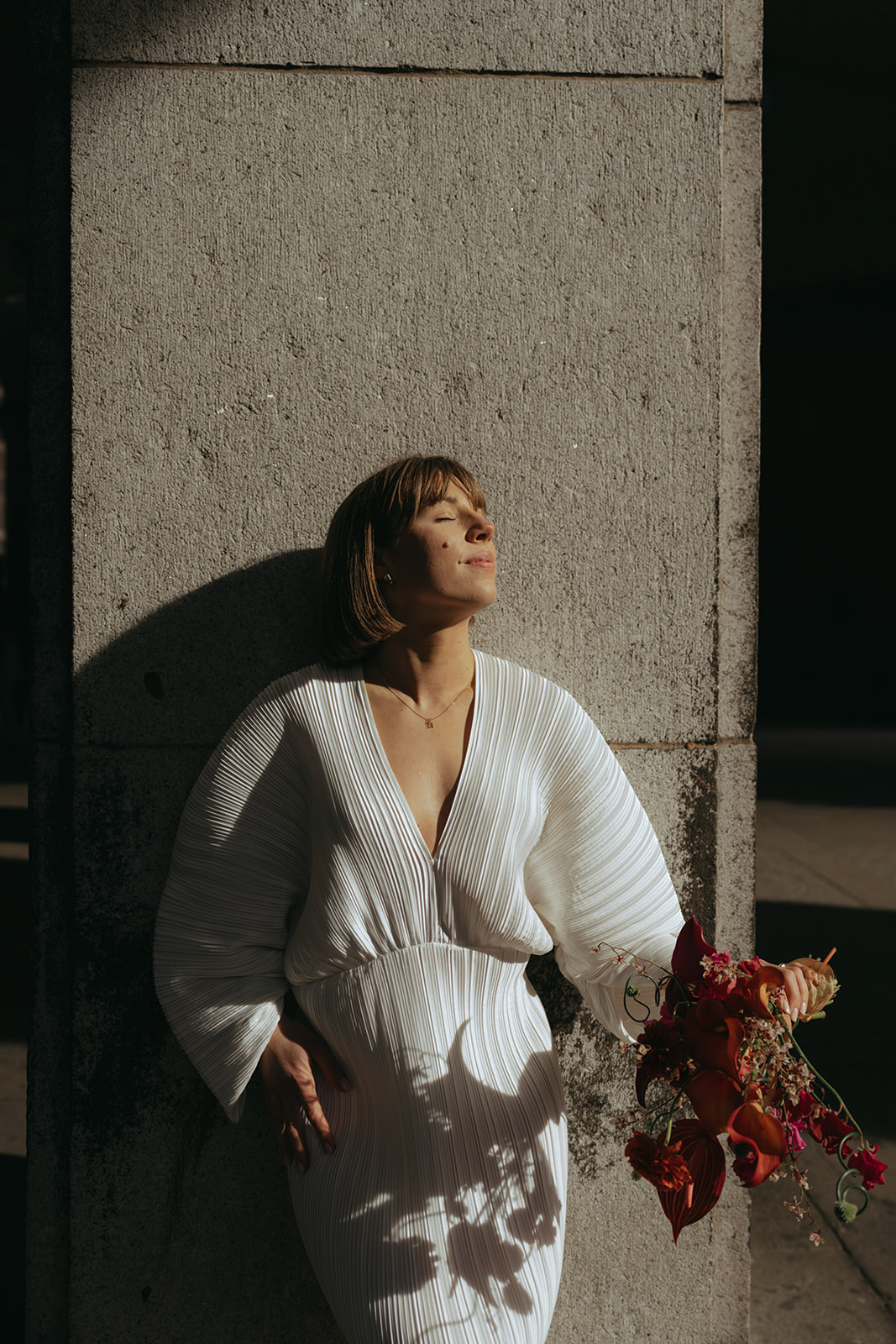 Rachel and Dave’s 2 day celebration Bride leaning up against a concrete column, tilting her face up towards the sun by NYC city hall wedding photographer Elsie Goodman.