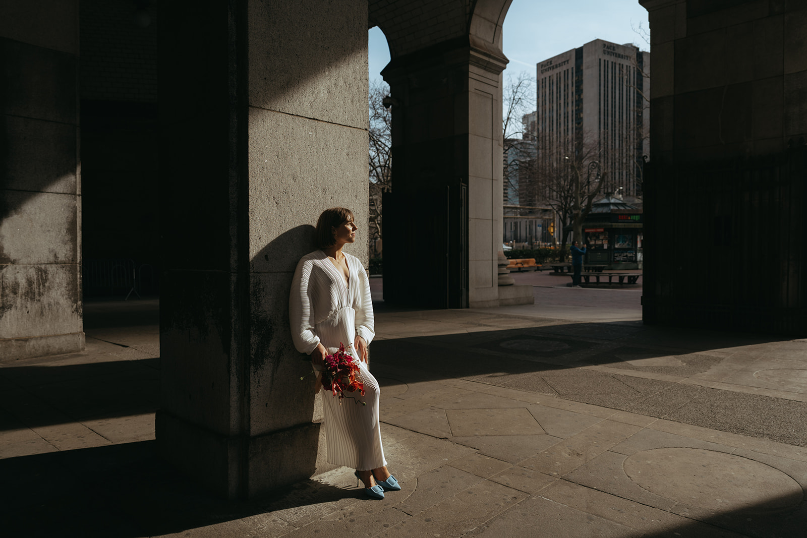 Rachel and Dave’s 2 day celebration Bride leaning up against big concrete columns by NYC city hall wedding photographer Elsie Goodman.