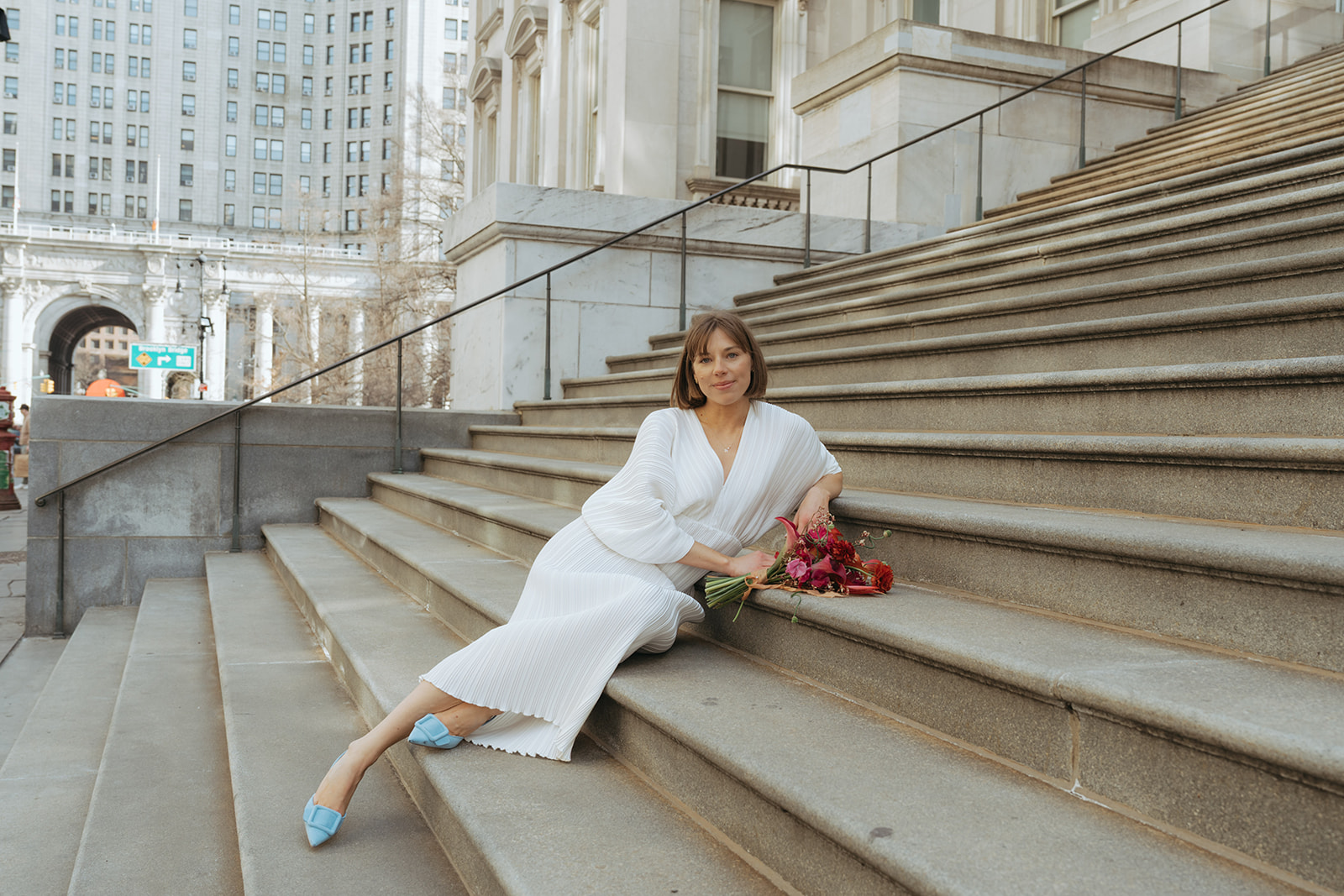 Rachel and Dave’s 2 day celebration Bride sits and leans against the stairs of city hall by NYC city hall wedding photographer Elsie Goodman.
