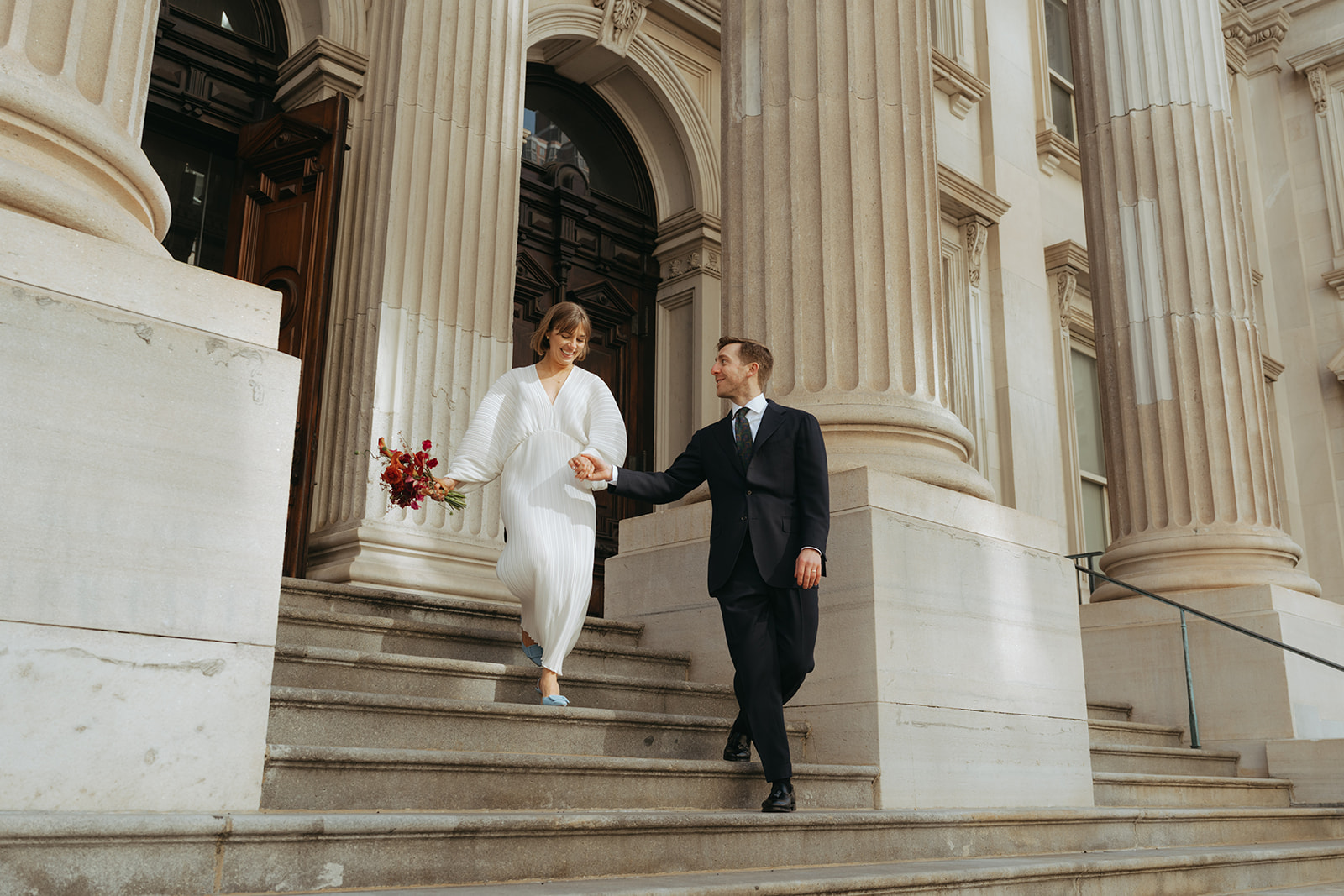 Rachel and Dave’s 2 day celebration Bride and groom walk down City Hall steps by NYC city hall wedding photographer Elsie Goodman.
