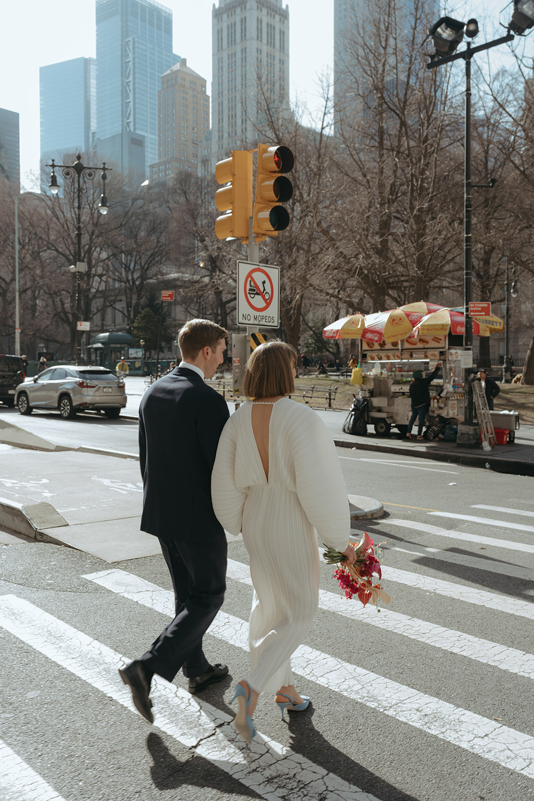 Rachel and Dave’s 2 day celebration Bride and groom walk hand in hand across a cross walk in NYC by NYC city hall wedding photographer Elsie Goodman.