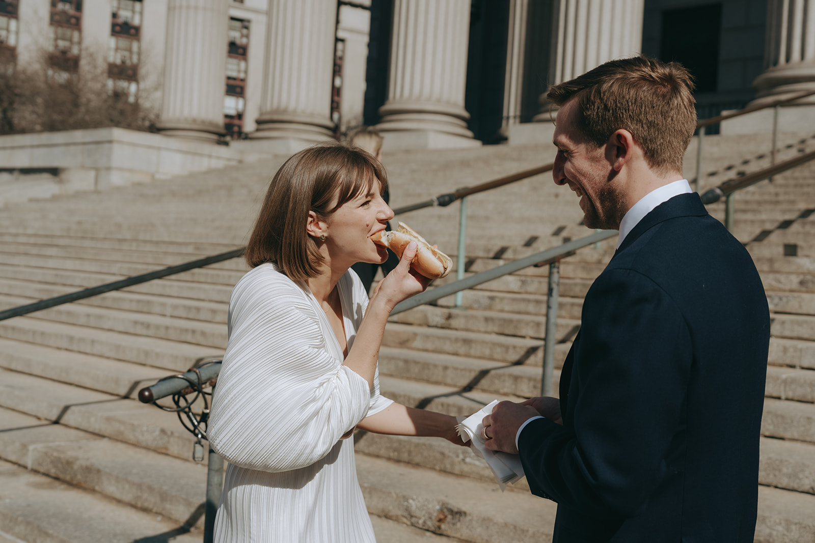Rachel and Dave’s 2 day celebration Bride in a vintage wedding dress biting into a hotdog, looking at her groom by NYC city hall wedding photographer Elsie Goodman.