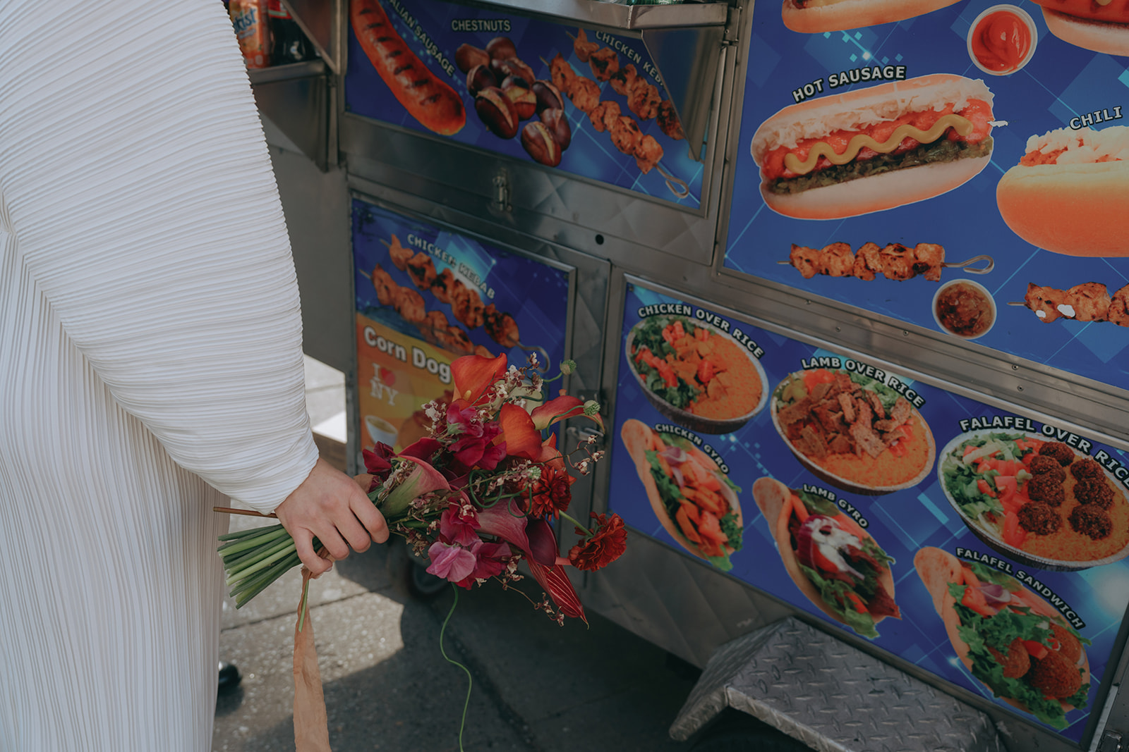 Rachel and Dave’s 2 day celebration Close up of a bride in a vintage wedding dress, you can see her colorful bouquet against a hot dog cart by NYC city hall wedding photographer Elsie Goodman.