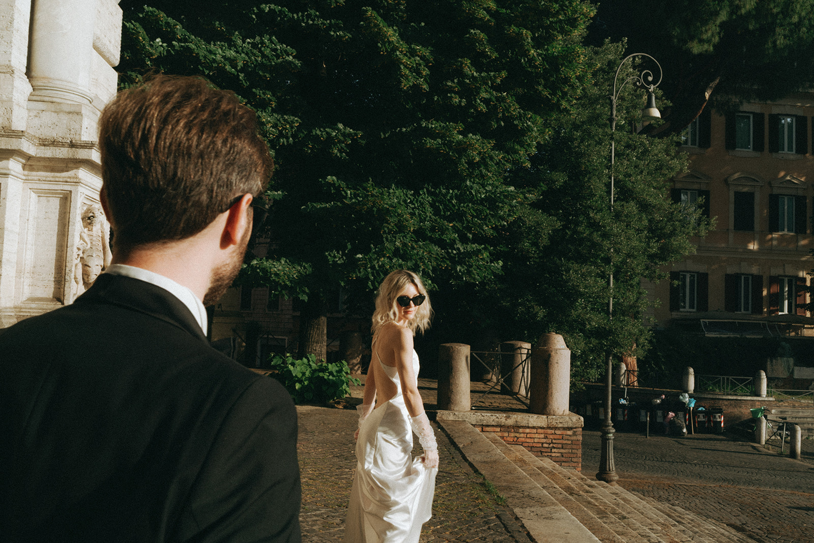 Over the shoulder shot of the groom as he looks at his bride walk away, the morning light is bright and golden by Rome elopement photographer Elsie Goodman.