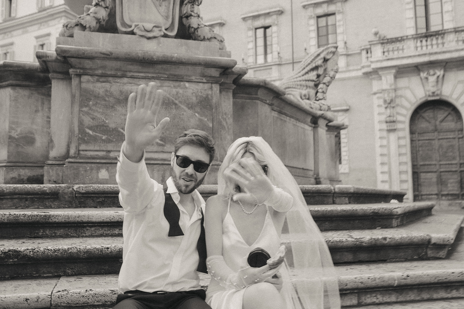 Bride and groom hold up their hands to the camera, covering their faces, Trastevere coffee shop by Rome elopement photographer Elsie Goodman.