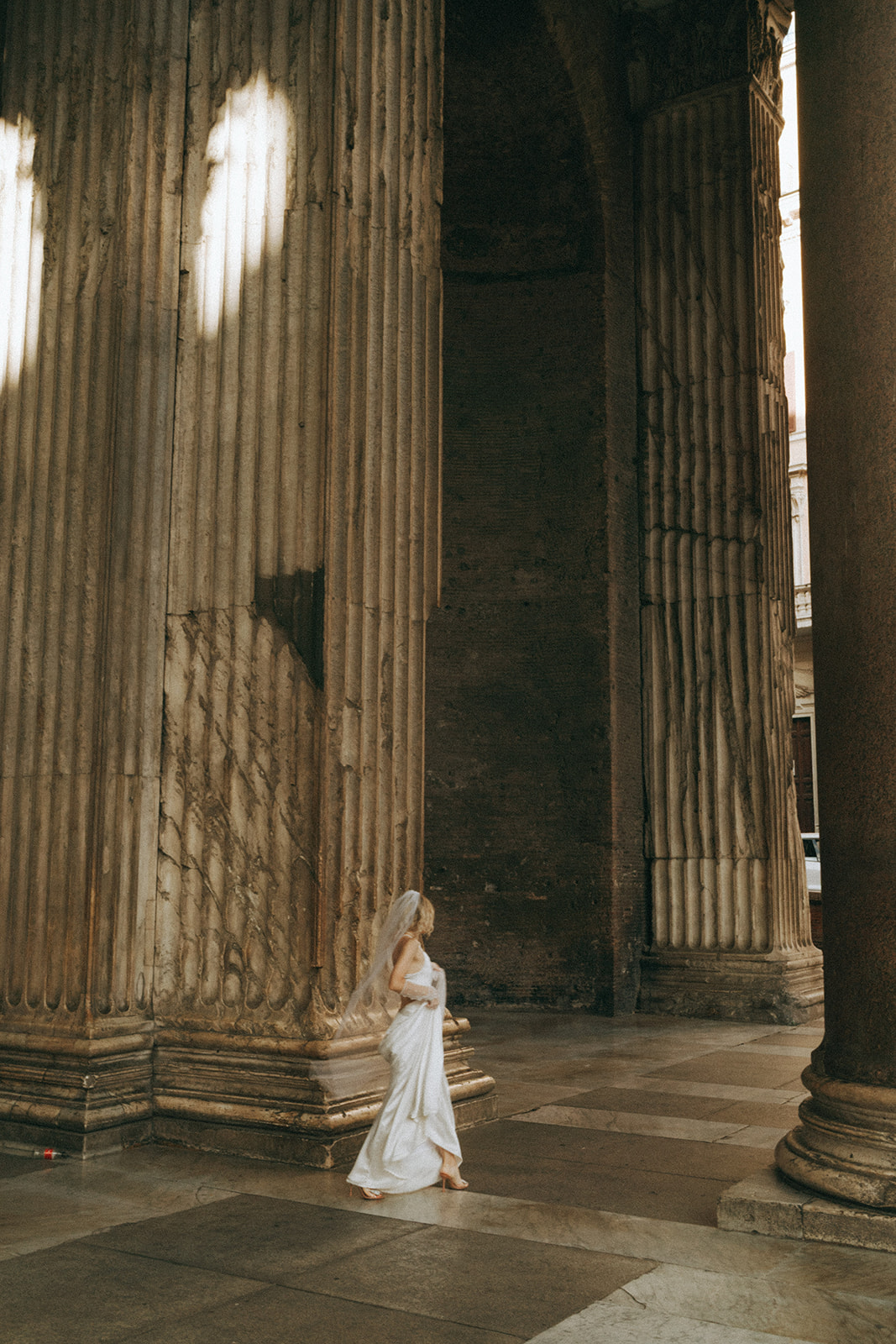 Bride in a white dress, veil and gloves walking among the columns of the Pantheon by Rome elopement photographer Elsie Goodman.