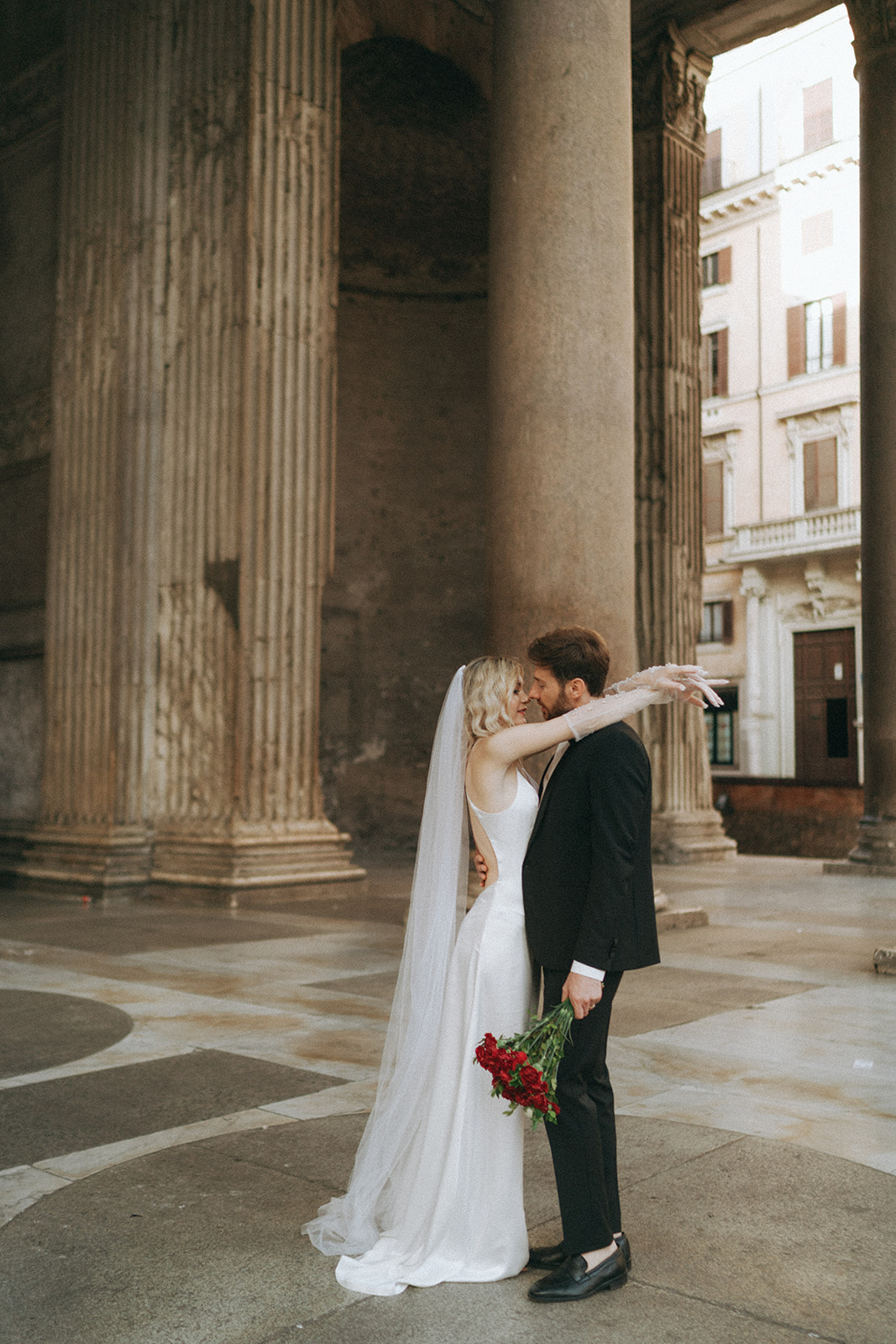 Bride with her arms around a groom under the columns of the Pantheon by Rome elopement photographer Elsie Goodman.