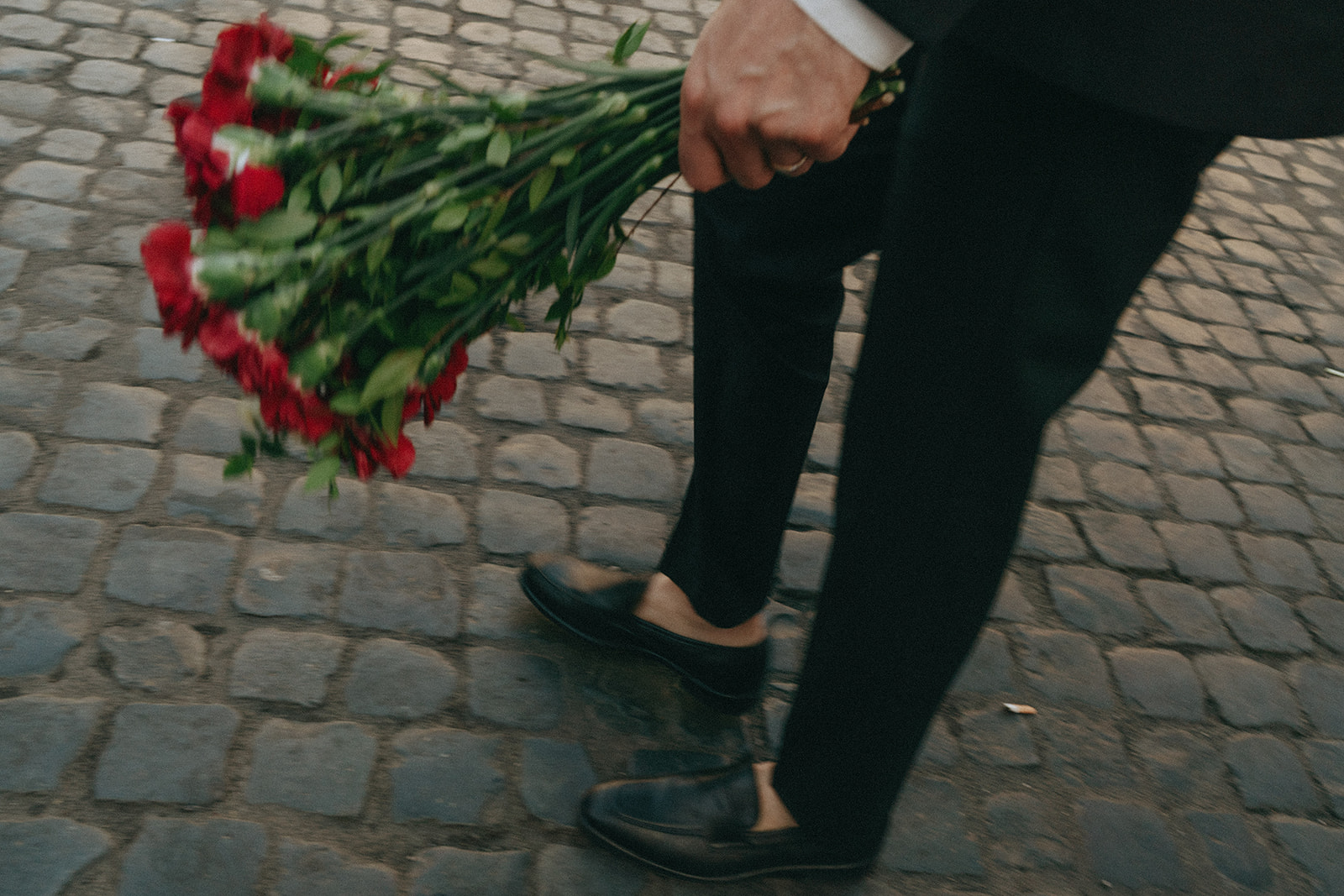 Action shot of the lower half of a groom holding the bouquet of red roses on cobblestone streets by Italy elopement photographer Elsie Goodman.