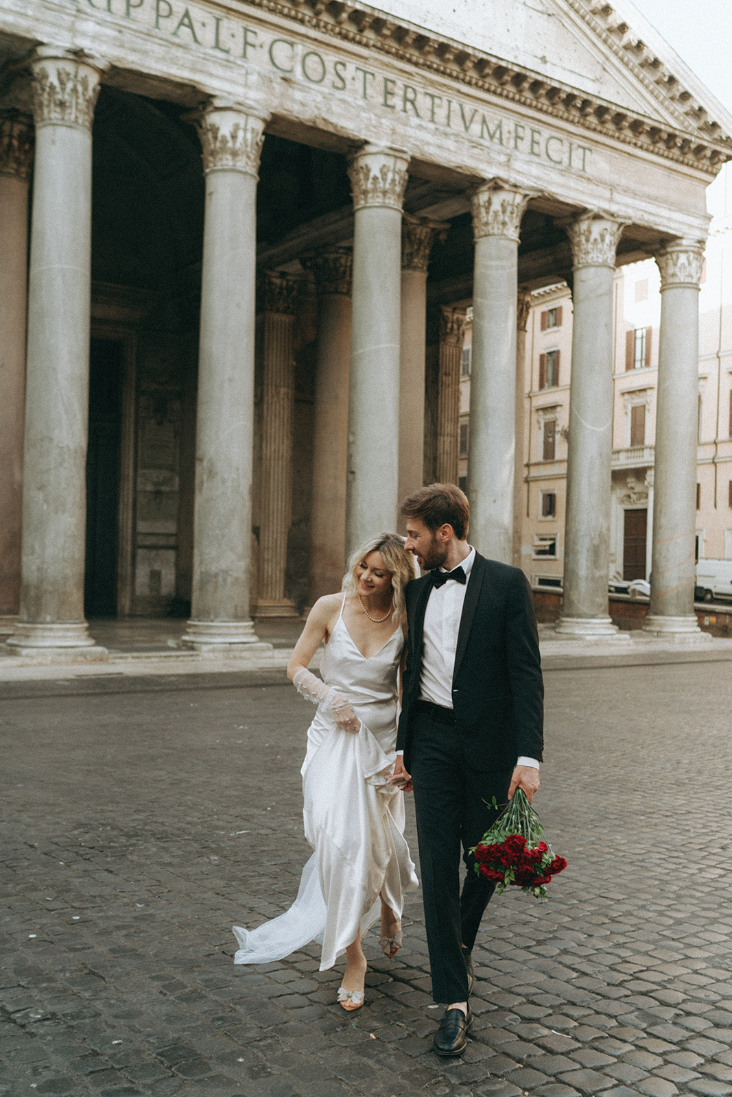 Bride and groom leaning in close to each other as they walk in front of the Pantheon by Italy elopement photographer Elsie Goodman.