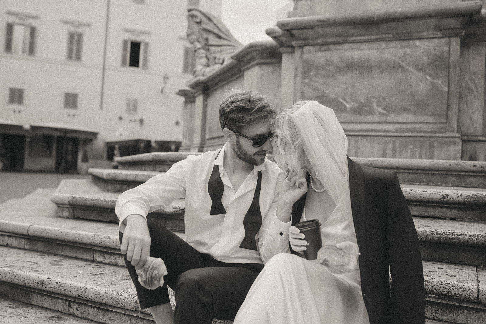 Groom leans in for a kiss from his bride, they are sitting on stone steps by Rome elopement photographer Elsie Goodman.
