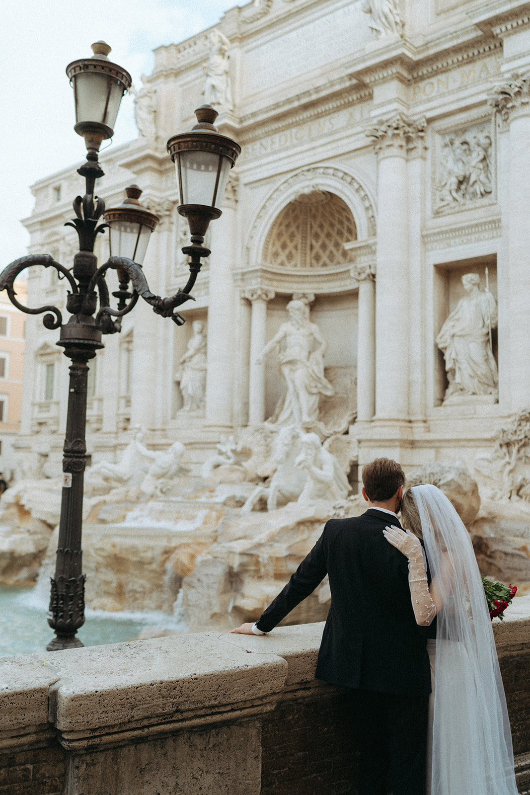 Shot of a bride and groom from behind as they overlook the Trevi Fountain at sunrise by Italy elopement photographer Elsie Goodman.