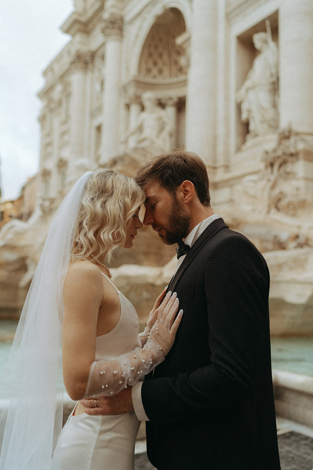 Bride and groom leaning towards each other, foreheads touching with the Trevi Fountain in the background by Italy elopement photographer Elsie Goodman.