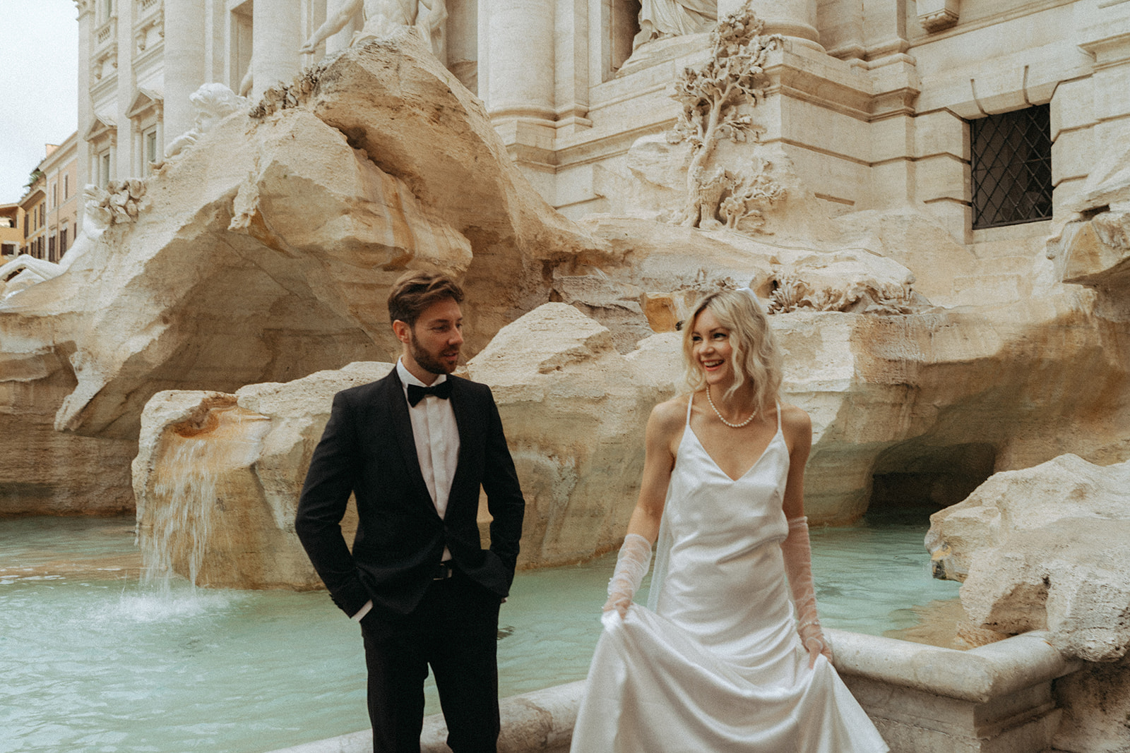 Bride and groom in front of a flowing Trevi Fountain at sunrise by Italy elopement photographer Elsie Goodman.