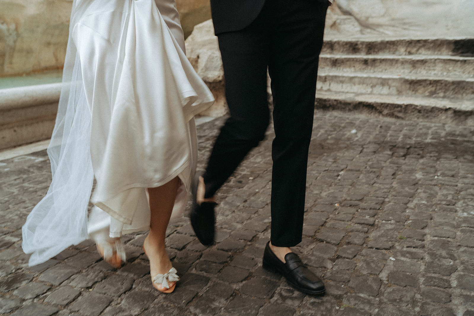 lower shot of a bride and groom walking on the cobblestone in front of the Trevi Fountain at sunrise by Italy elopement photographer Elsie Goodman.