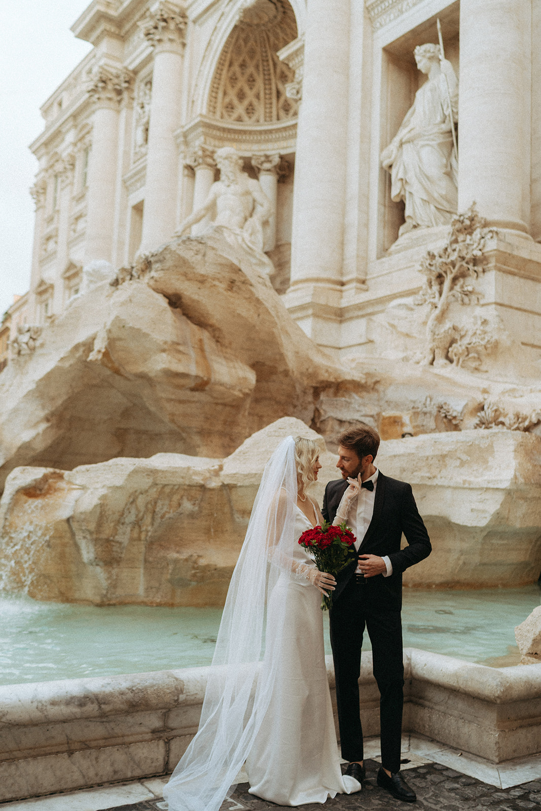Bride and groom looking lovingly at each other in front of the Trevi Fountain at sunrise by Italian elopement photographer Elsie Goodman.